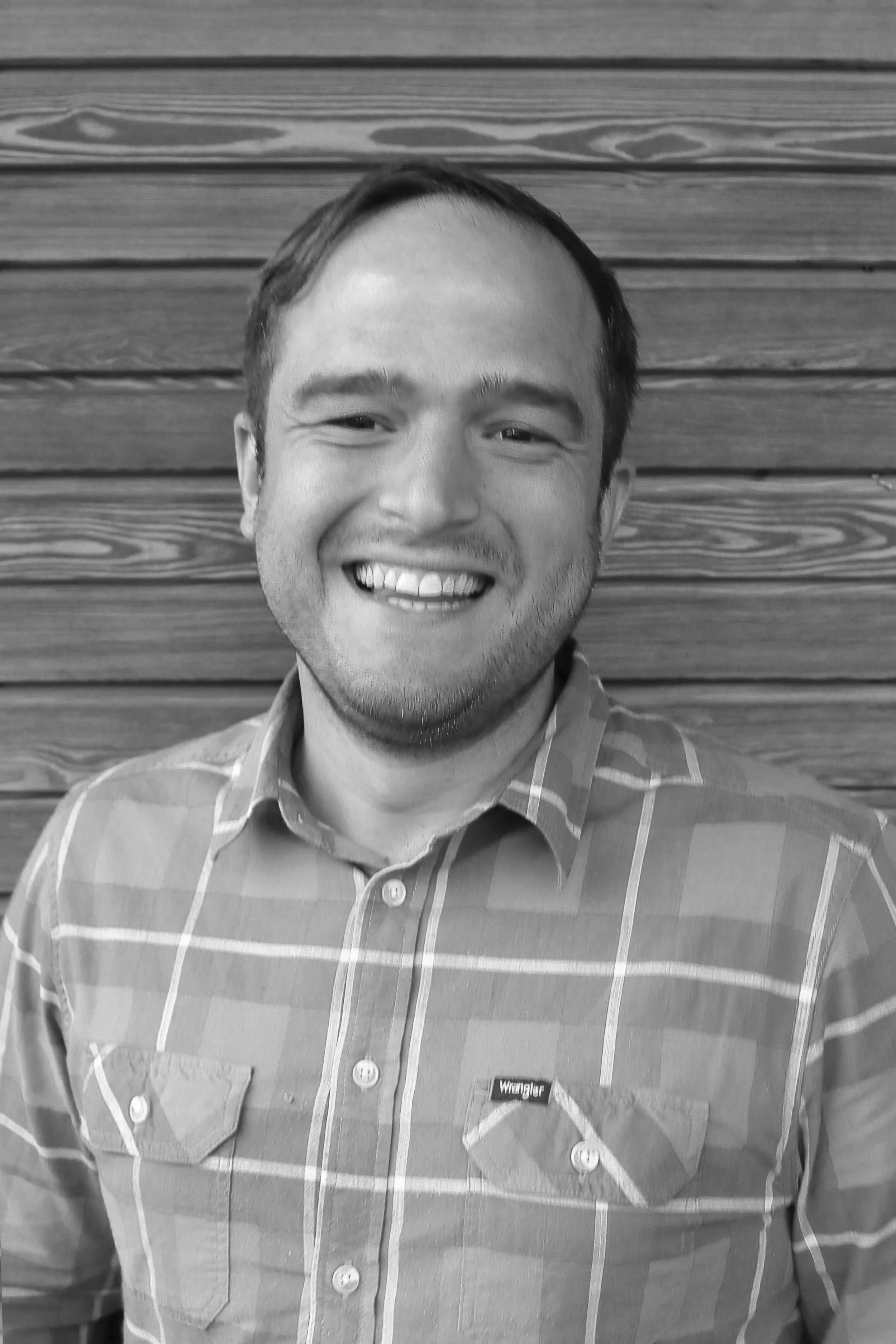 Schwarz-Weiß-Foto eines lachenden Mannes vor einer Holzvertäfelung