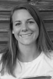 Ein Porträt einer lachenden jungen Frau vor Holzverkleidung im Schwarz-Weiß.