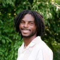 Portrait of a young man smiling outdoors against green foliage.