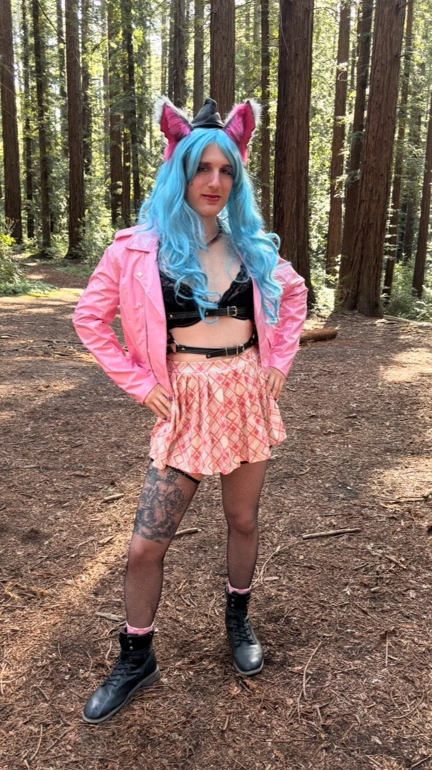 Queer Reiki healer with blue hair wearing a leather jacket and harness, standing powerfully, in a Redwood forest