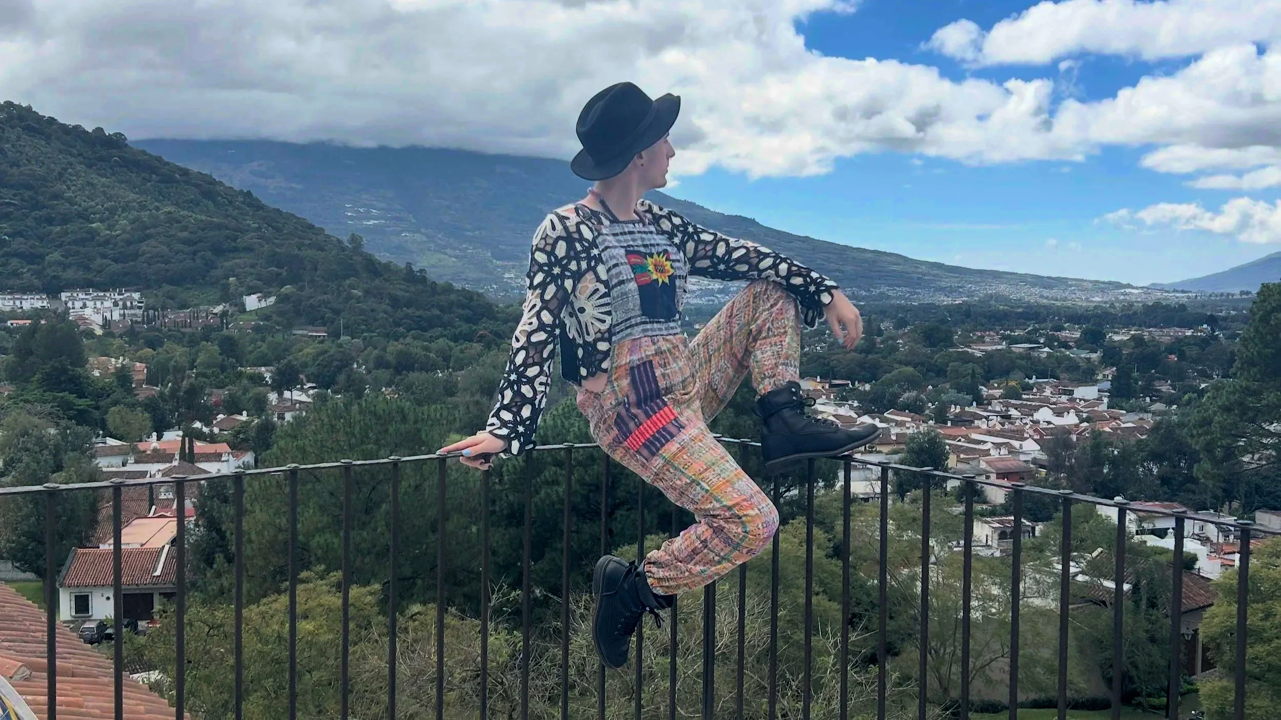 Transwoman sitting on a railing dressed in Guatemalan textiles looking out at Antigua, Guatemala