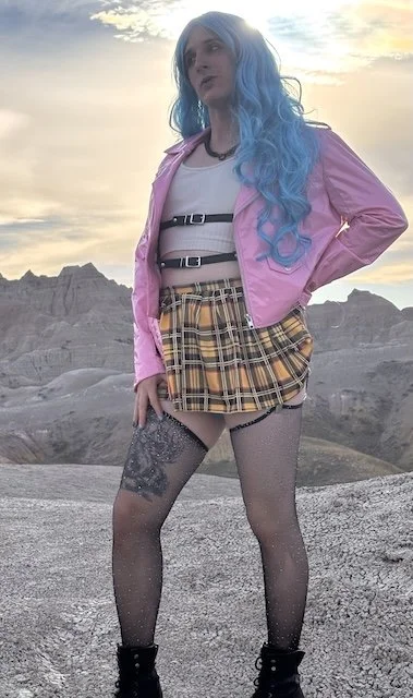 Reiki practitioner with blue hair posing in a leaather jacket, leather harness, and skirt at sunset in Badlands National Park