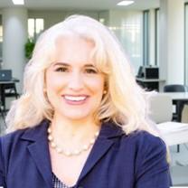 Portrait of a smiling woman with blonde hair in a modern office setting.