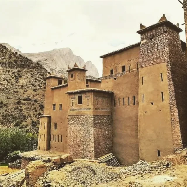 Ancient desert fortress with mud-brick walls, towers, and small windows, built against a mountainous landscape.