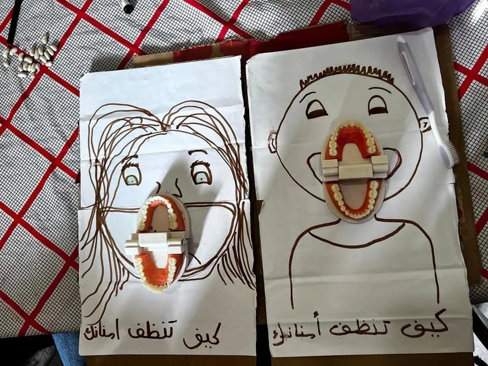 Two drawings of people with dental models in their mouths, on white paper, with Arabic writing. The left drawing is of a girl with long hair; the right is of a boy with short hair.