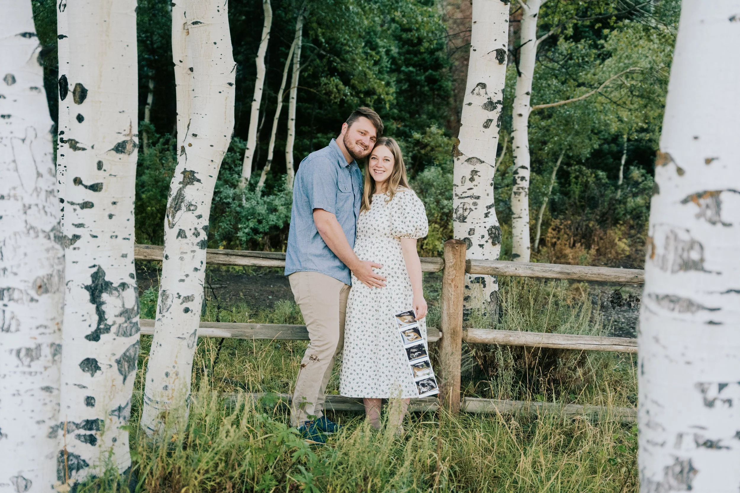 Photo of couple leaning against a fence holding a baby ultrasound.