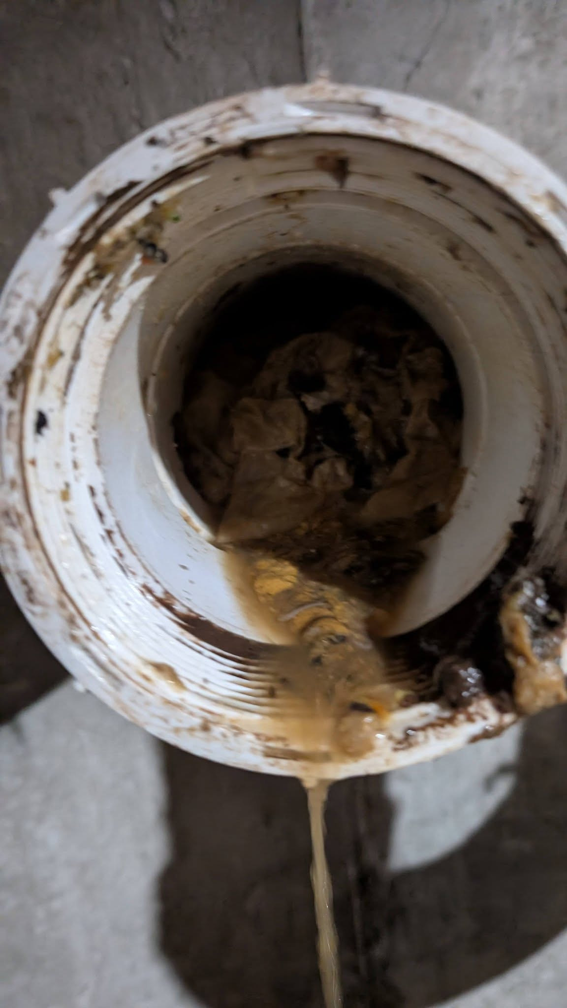 Close-up of an open pipe or drain with dirty, muddy water and debris inside, with some water dripping or flowing out.
