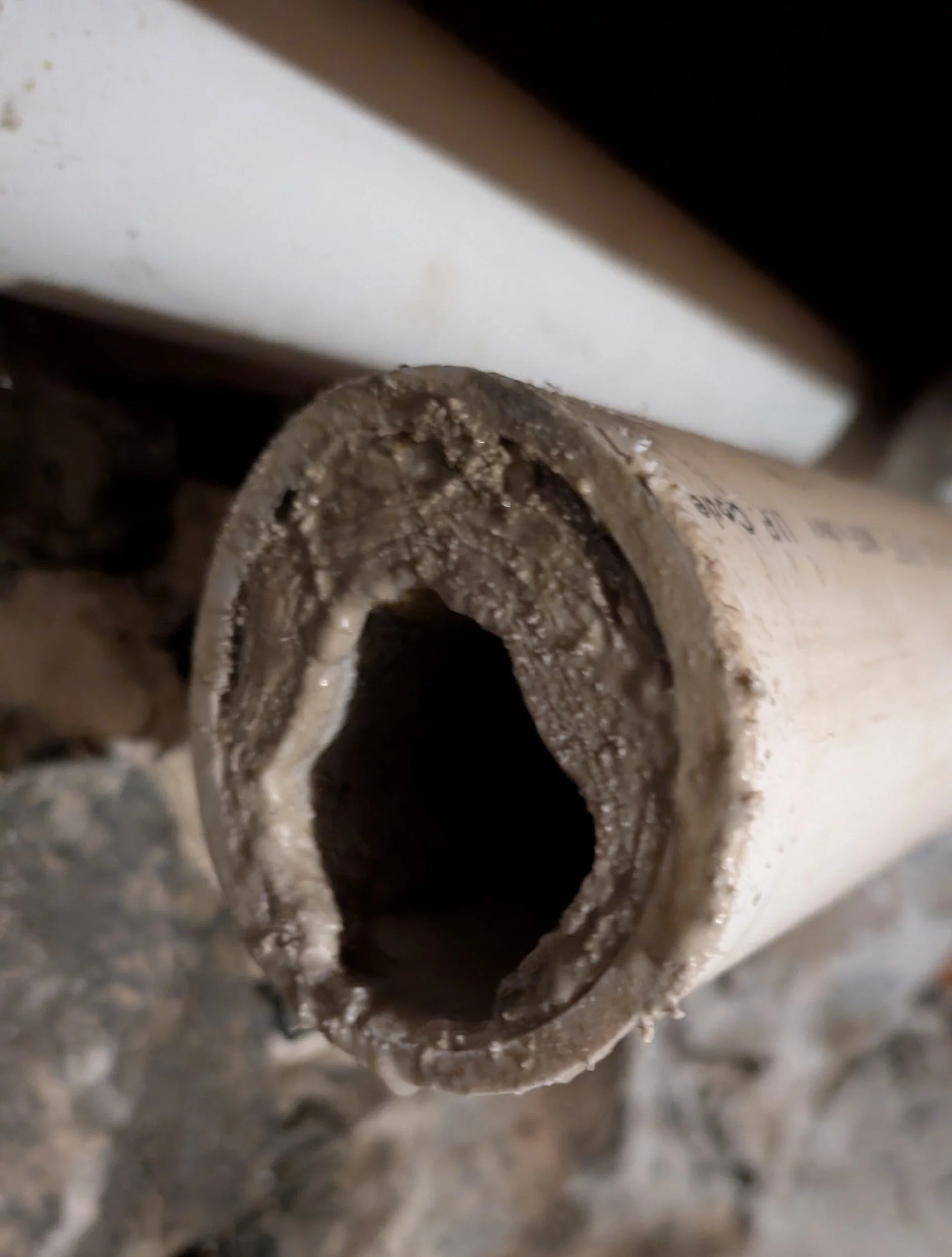 Close-up of a dirty, hollow PVC pipe lying on a rough surface with debris.