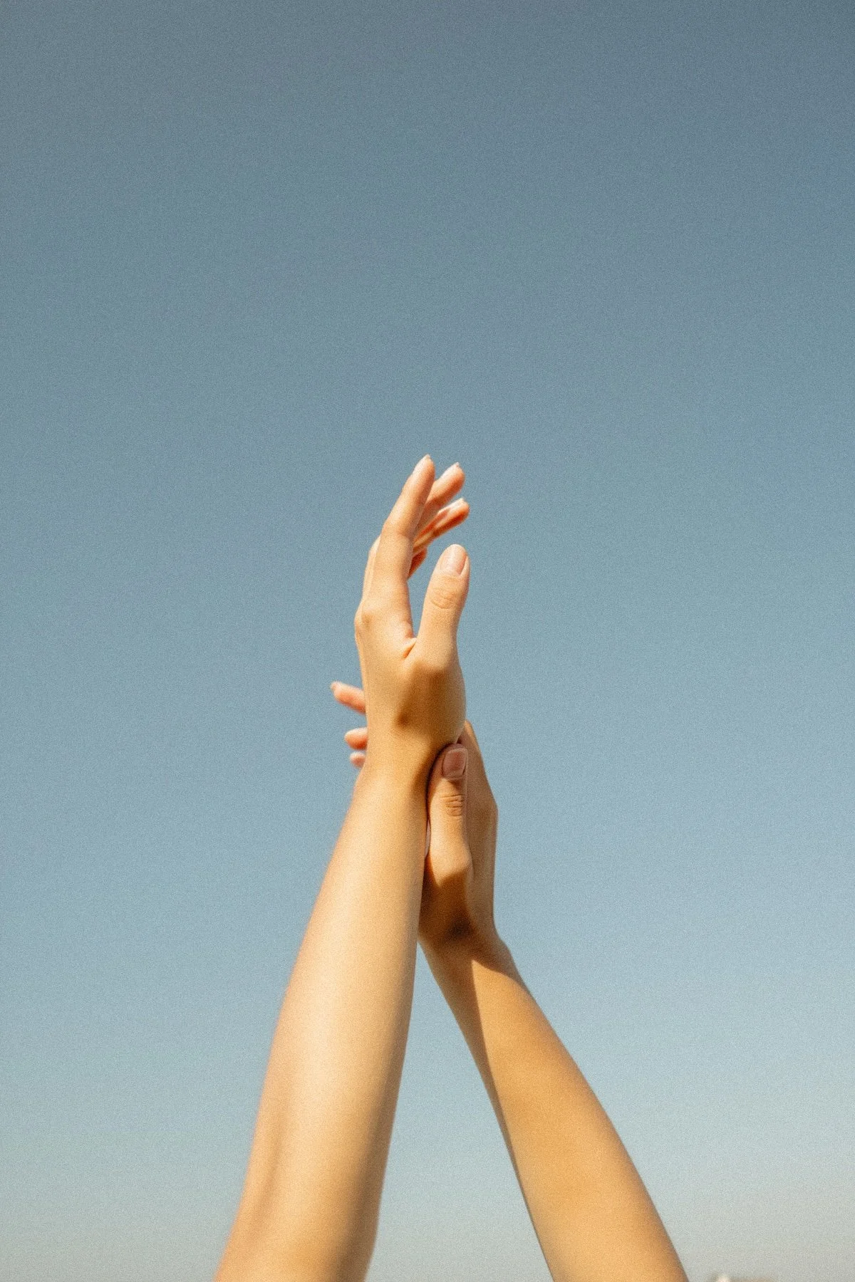 Zwei Hände, die sich unter einem klaren Himmel berühren.