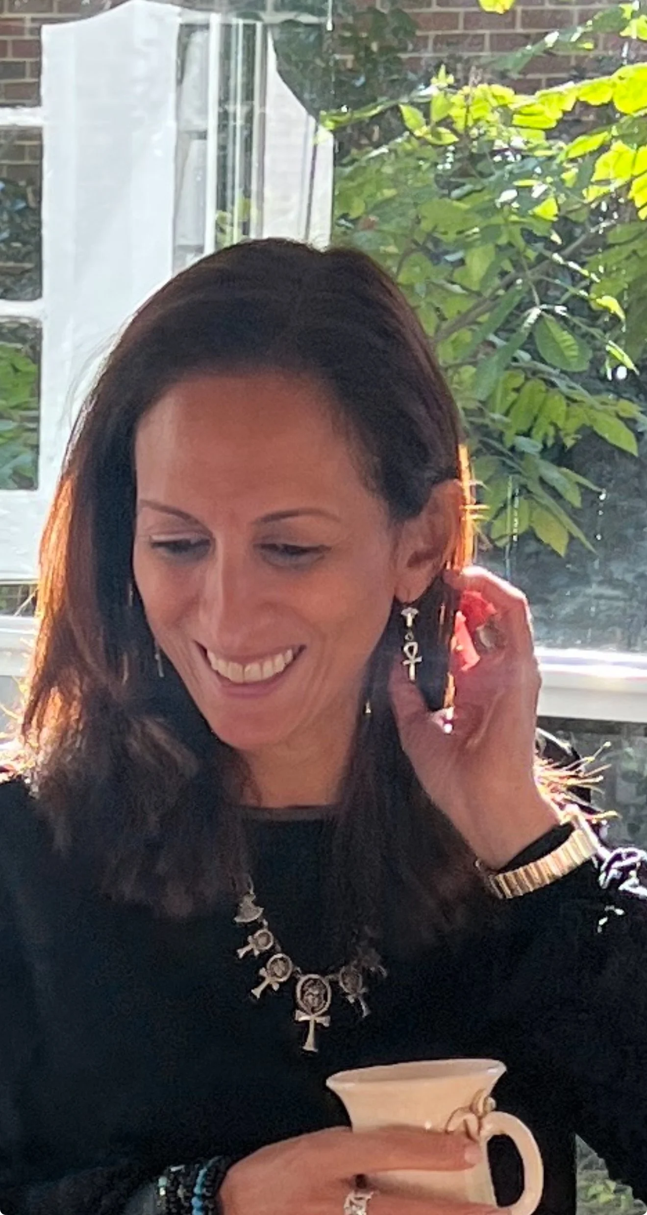 A woman with shoulder-length and silver jewelry smiles and looks down, away from the camera