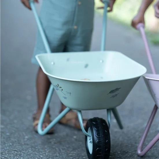 Children pushing toy wheelbarrows outdoors on a paved path.