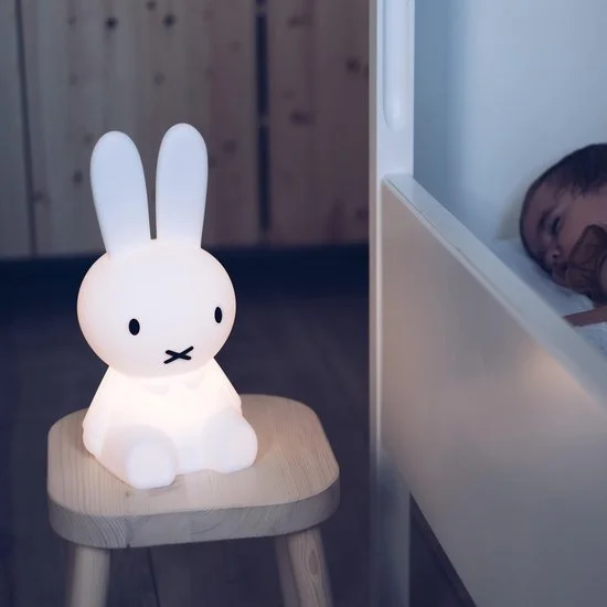 A white, bunny-shaped night light sitting on a small wooden stool in a room.