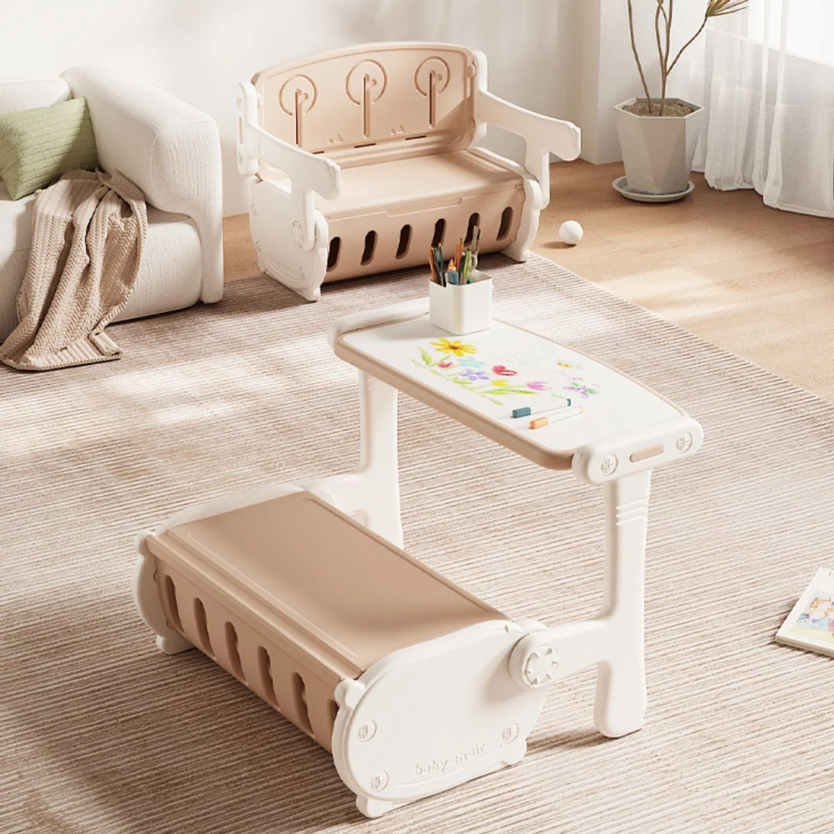 A children's room with a white bookshelf, wooden bench, small white table with colorful drawings and markers, a white sofa with a green cushion and knitted blanket, a potted plant, and a textured beige rug.