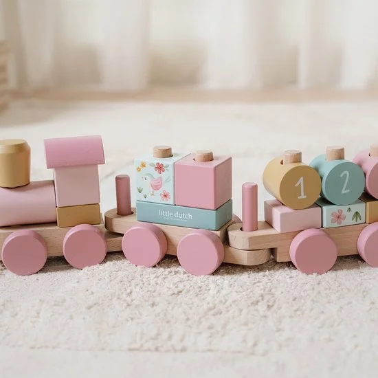 Colorful wooden toy train with pastel pink, blue, and yellow blocks on a plush carpet in a bright room.