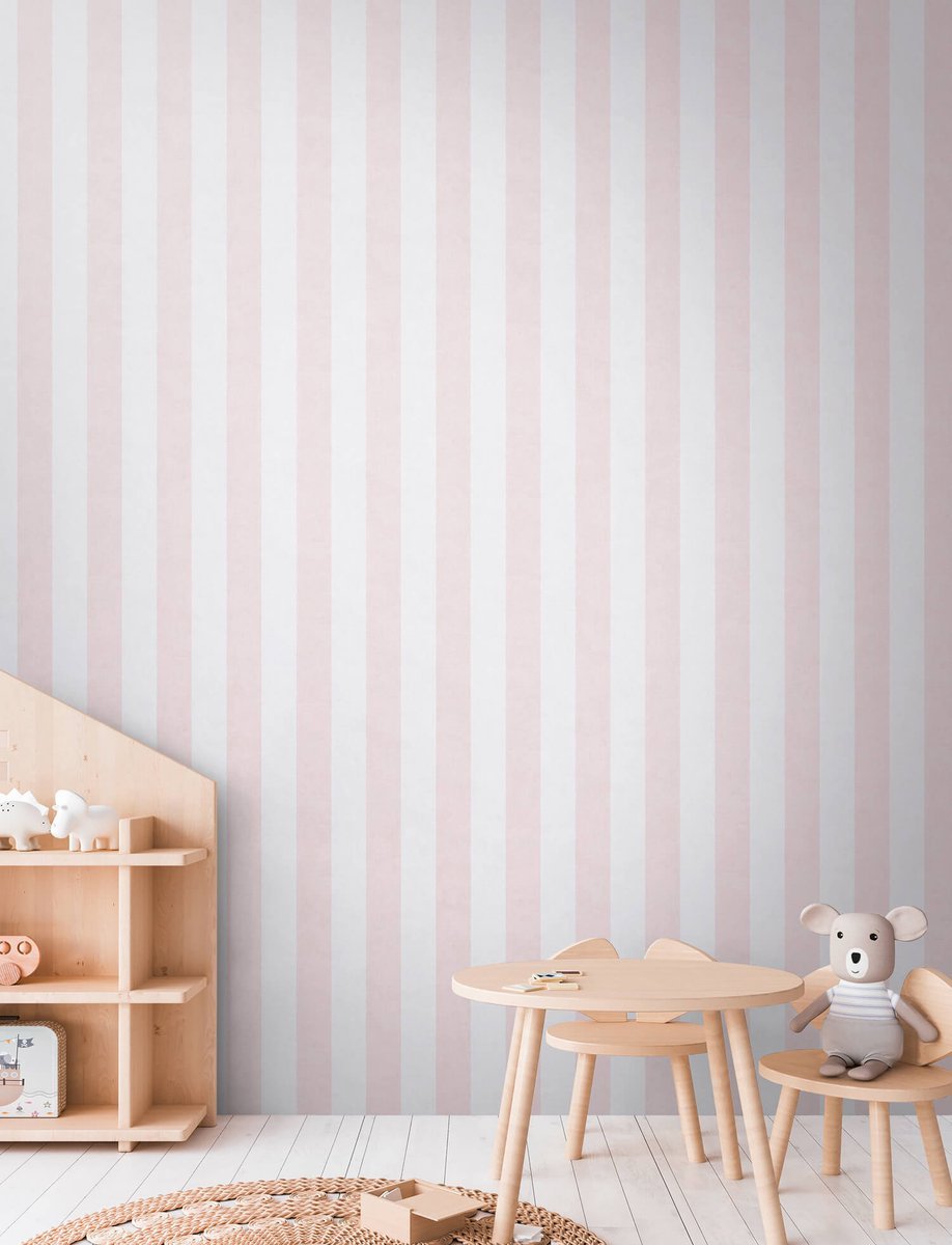 A corner of a children's room with pink and white vertical striped wallpaper, a small round wooden table, two wooden chairs, and plush toys including a teddy bear and other animal figures.