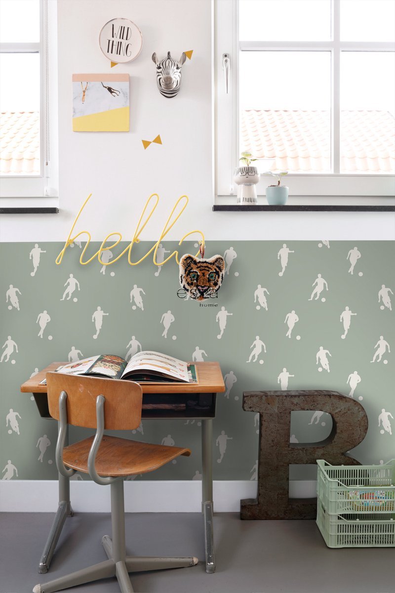 A children’s study area with a wooden desk and chair, a decorative wall with animal-themed decor, the word 'hello' in yellow script, and a large letter 'R' on the floor. There are potted plants on the window sill and a basket of books.