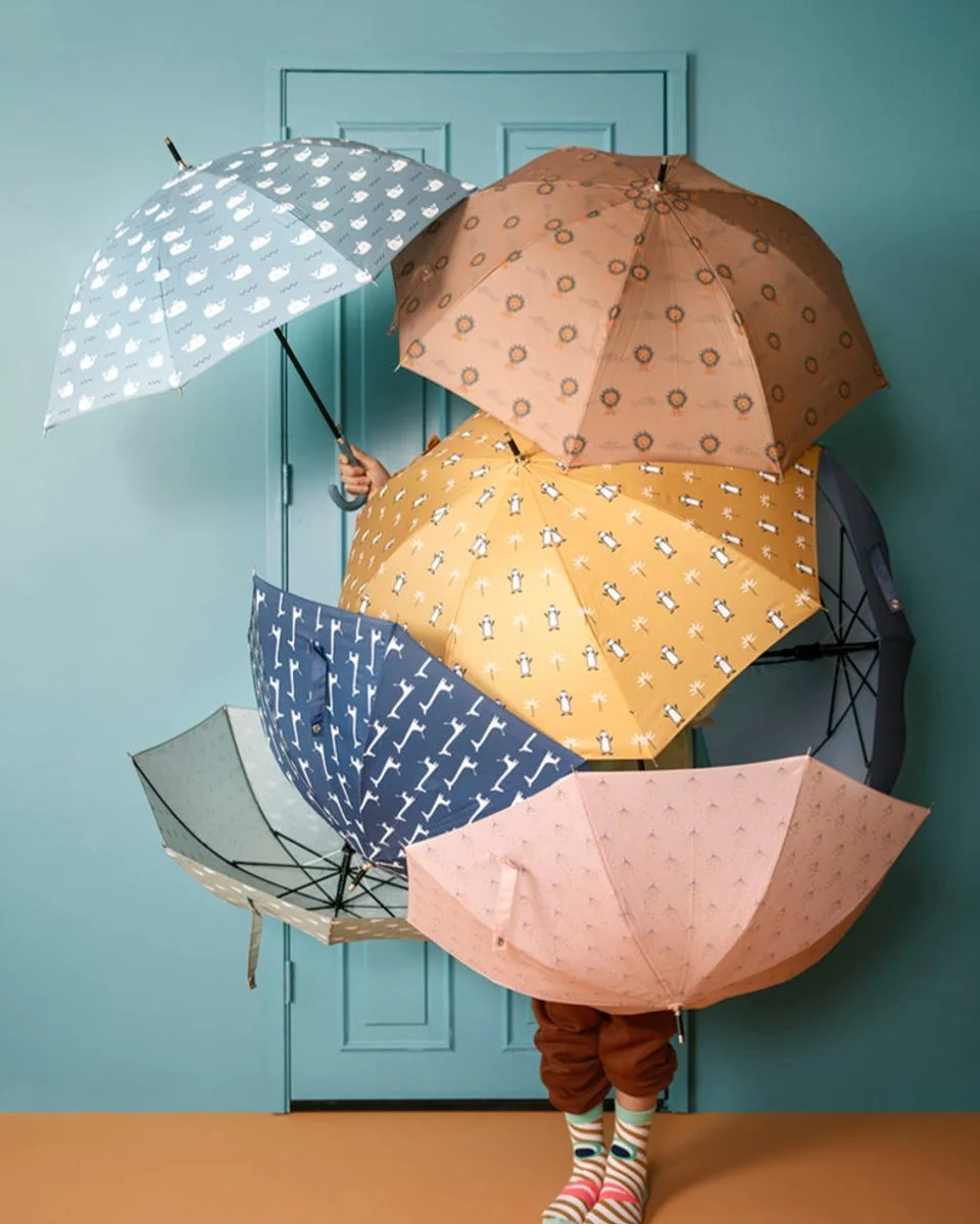 Person holding six colorful umbrellas, standing behind a blue door, with only their legs and striped socks visible.