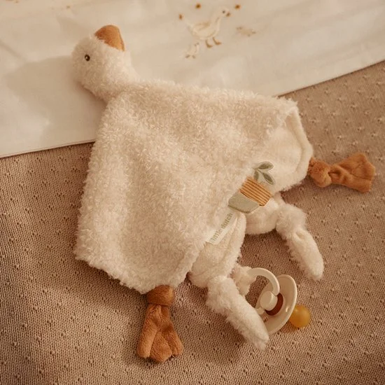 A plush stuffed animal resembling a white bird with a beige beak, wings, and feet. It has a fluffy towel draped over its back and a pacifier attached to its leg.