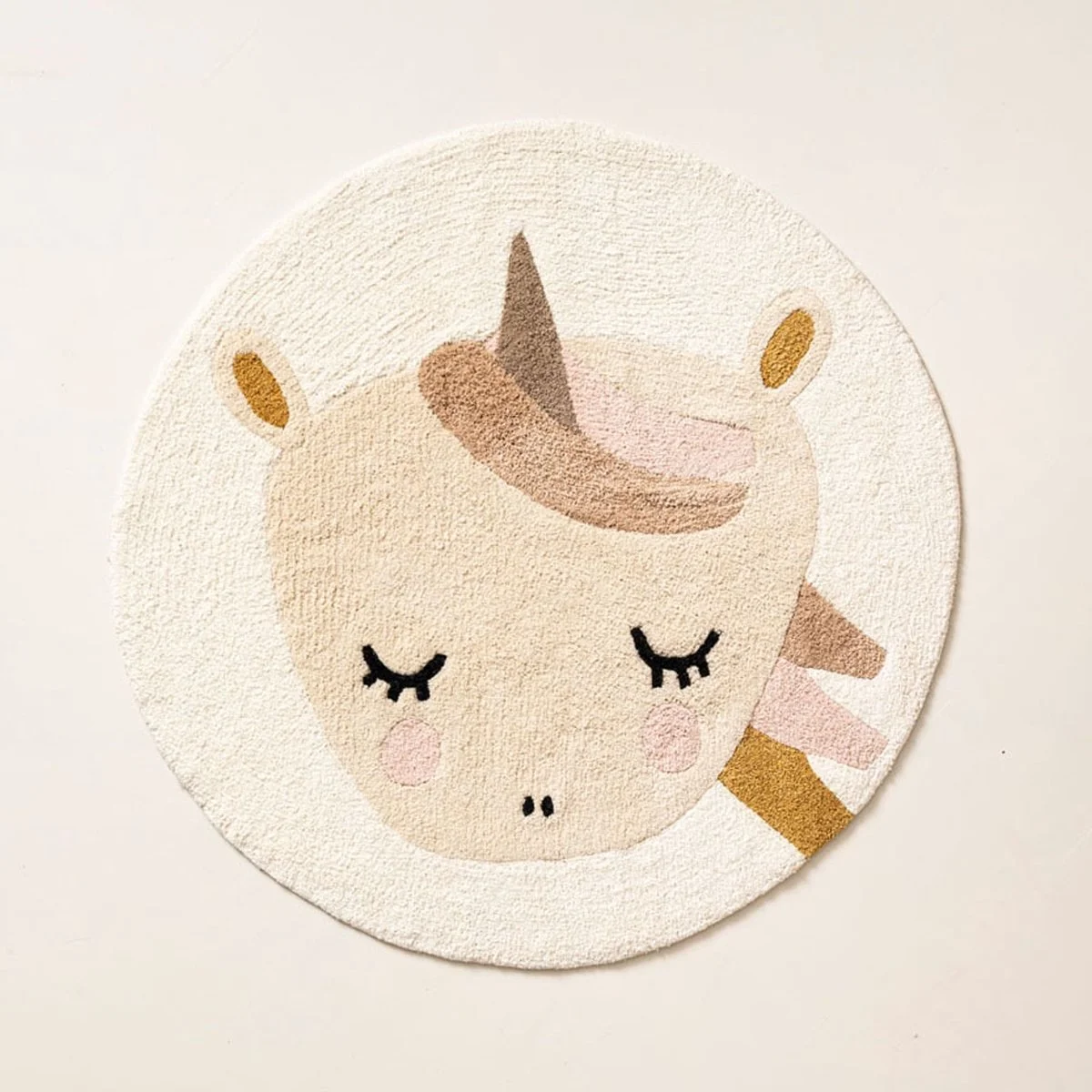 Round rug with a cute unicorn face featuring closed eyes and a rainbow-colored mane in pastel shades.