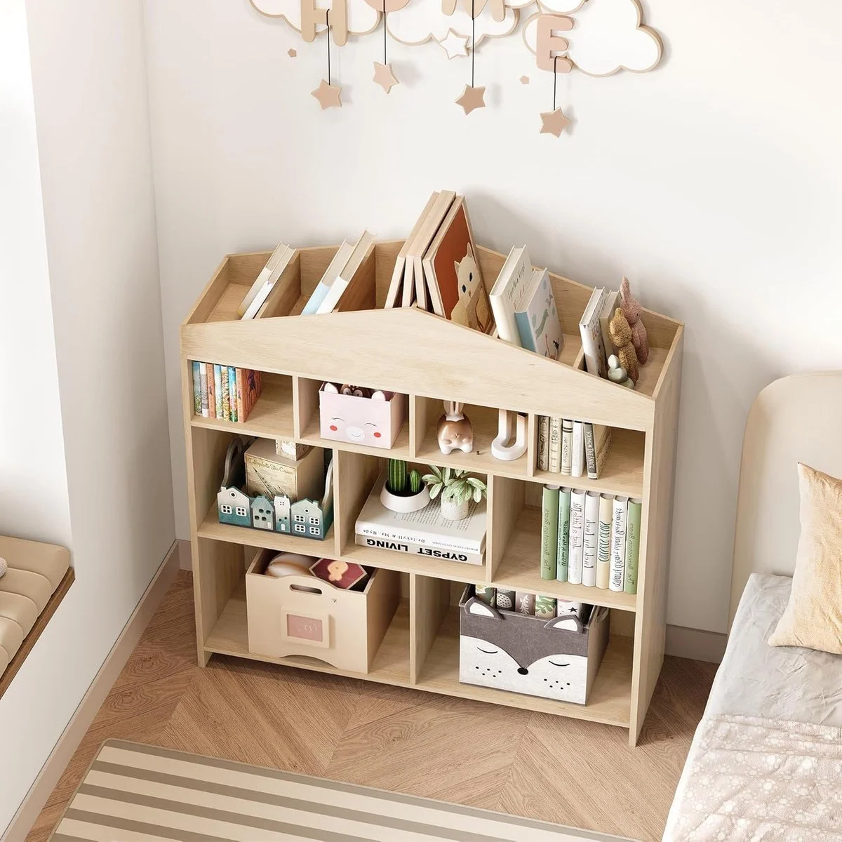 Wooden bookshelf with children's books, toys, and decorative items against a white wall with hanging cloud and star decor.