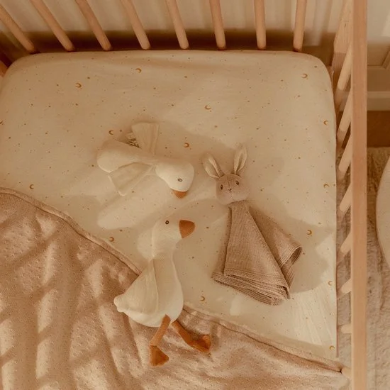 Two stuffed animal toys, a duck and a rabbit, lying on a crib mattress with a blanket.
