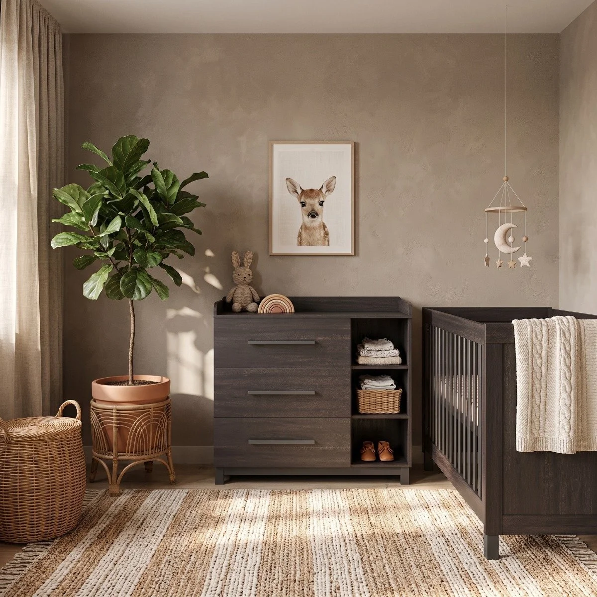 A nursery with a large potted fiddle leaf fig tree, a rattan basket, a dark wood dresser with stuffed bunny and rainbow decor, a framed picture of a deer, a hanging moon and star mobile, and a dark wooden crib with a white knitted blanket, all illuminated by natural light from a window.