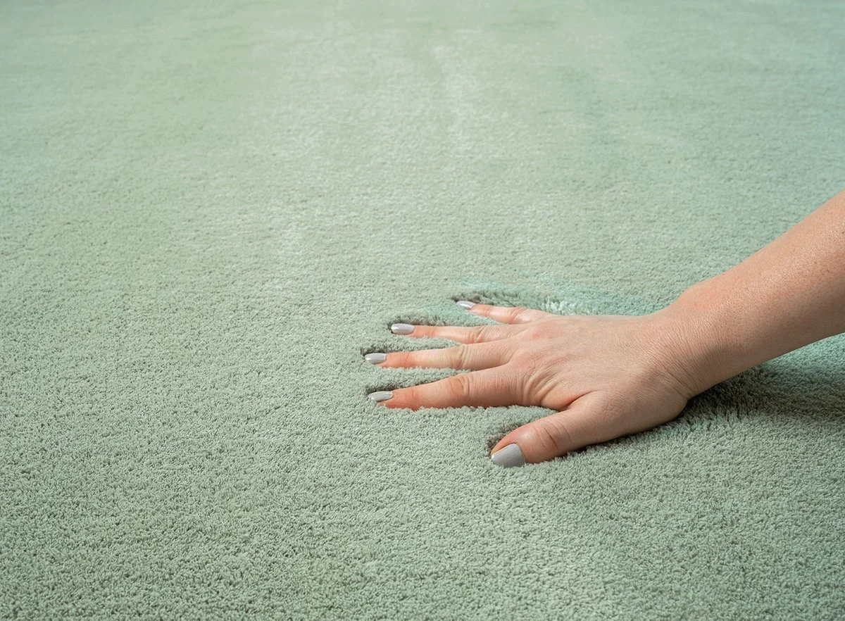 Close-up of a person's hand smoothing out a green carpet.