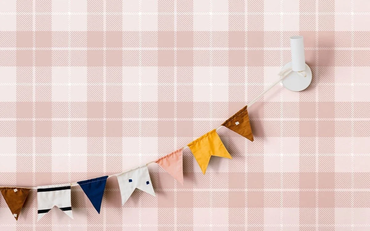 Colorful fabric bunting hung on a pink plaid patterned wall.