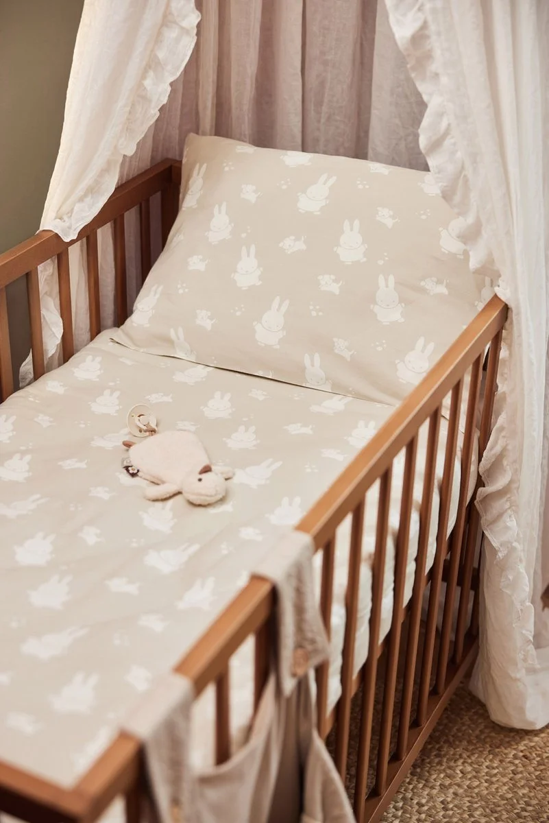 A baby crib with bunny-themed bedding and a stuffed bunny toy, surrounded by white curtains.