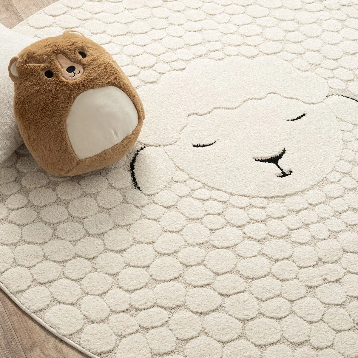 A plush bear-shaped pillow and a cream-colored rug with a sleeping bear face design on a wooden floor.