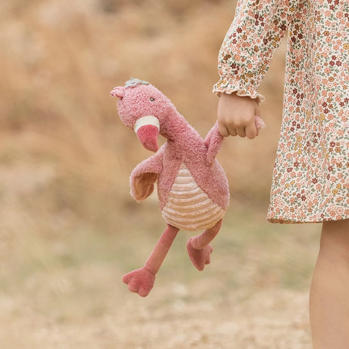 A child holding a pink stuffed animal resembling a dragon or dinosaur outside on a blurred natural background.