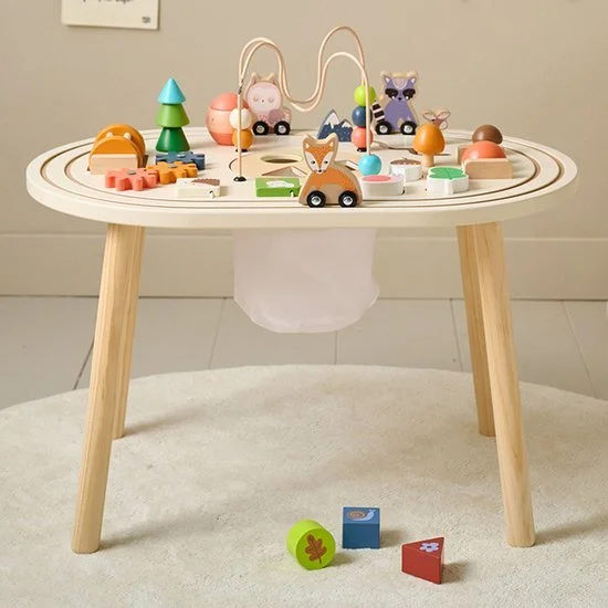 A wooden children's play table with a bead maze and various colorful wooden animal and nature-themed toys on it, with additional small toys on the floor in front of it.
