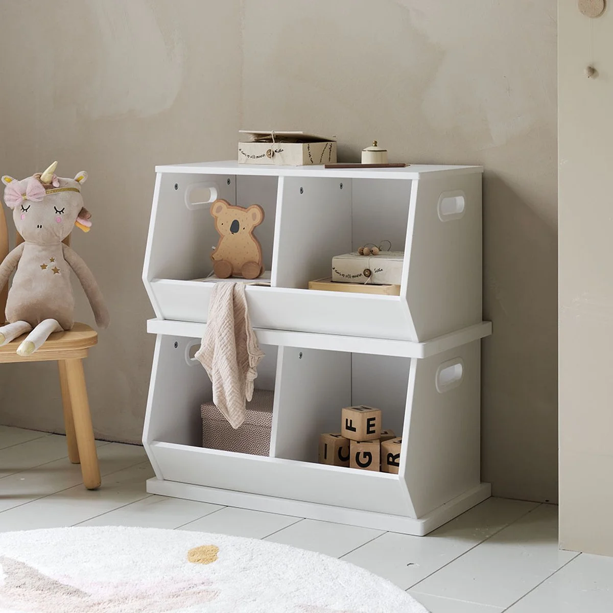A white children's storage shelf with open compartments, decorated with toys and storage boxes, next to a plush unicorn doll on a wooden stool.