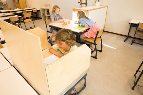 Three young girls studying at school desks in a classroom.