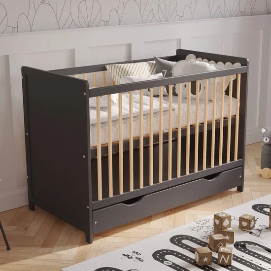 Black and wooden crib with a white and gray mattress and pillows, in a child's nursery with a patterned wall and a play rug with toy blocks.