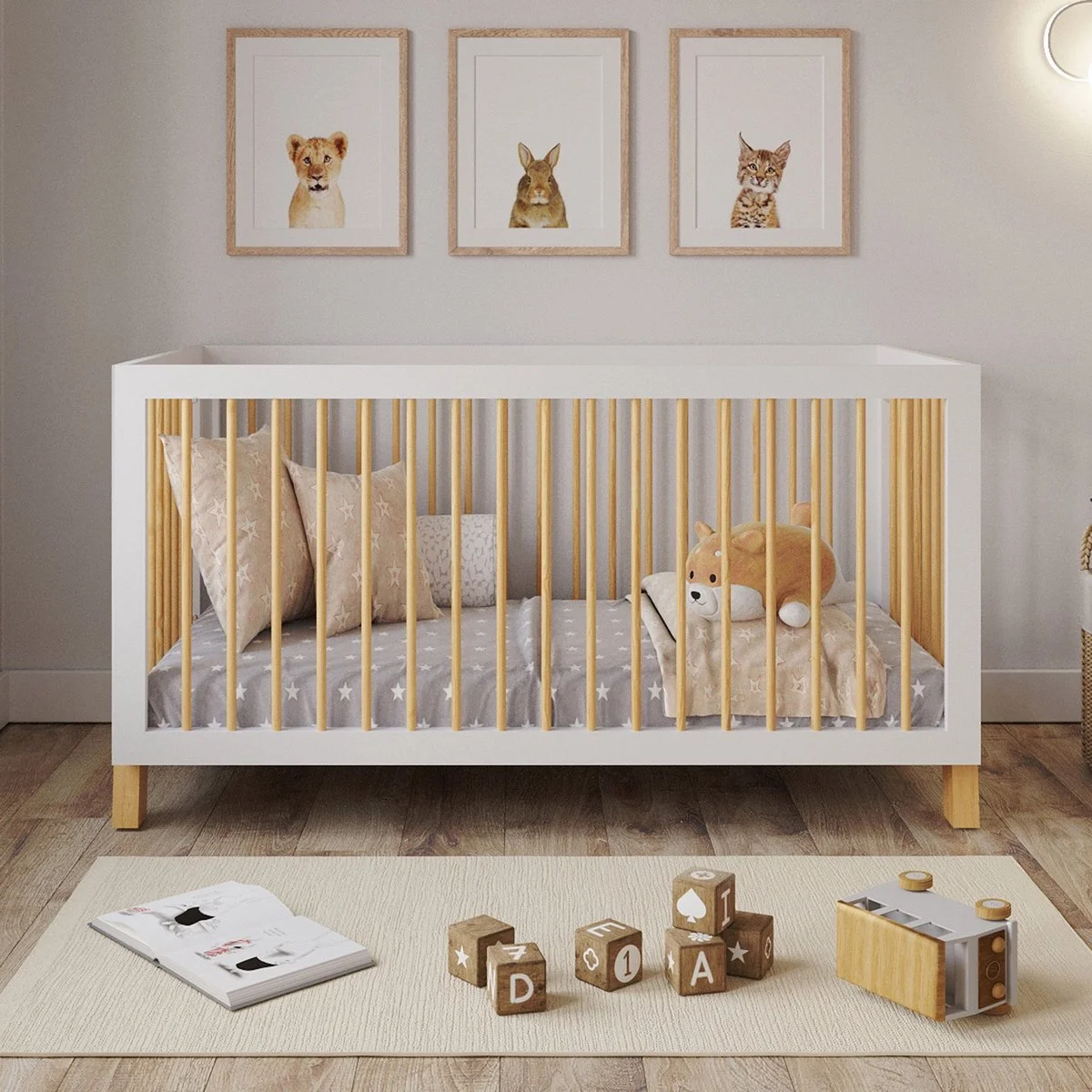 Nursery with white crib that has wooden bars, a plush dog toy inside, star-patterned bedding, and three star-patterned pillows. On the wall above, three framed animal illustrations of a lion, a rabbit, and a cat. Wooden alphabet blocks and a toy camera on a white rug in front of the crib.
