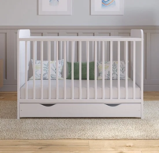 White crib with pillows inside, set in a nursery with framed artwork on the wall.