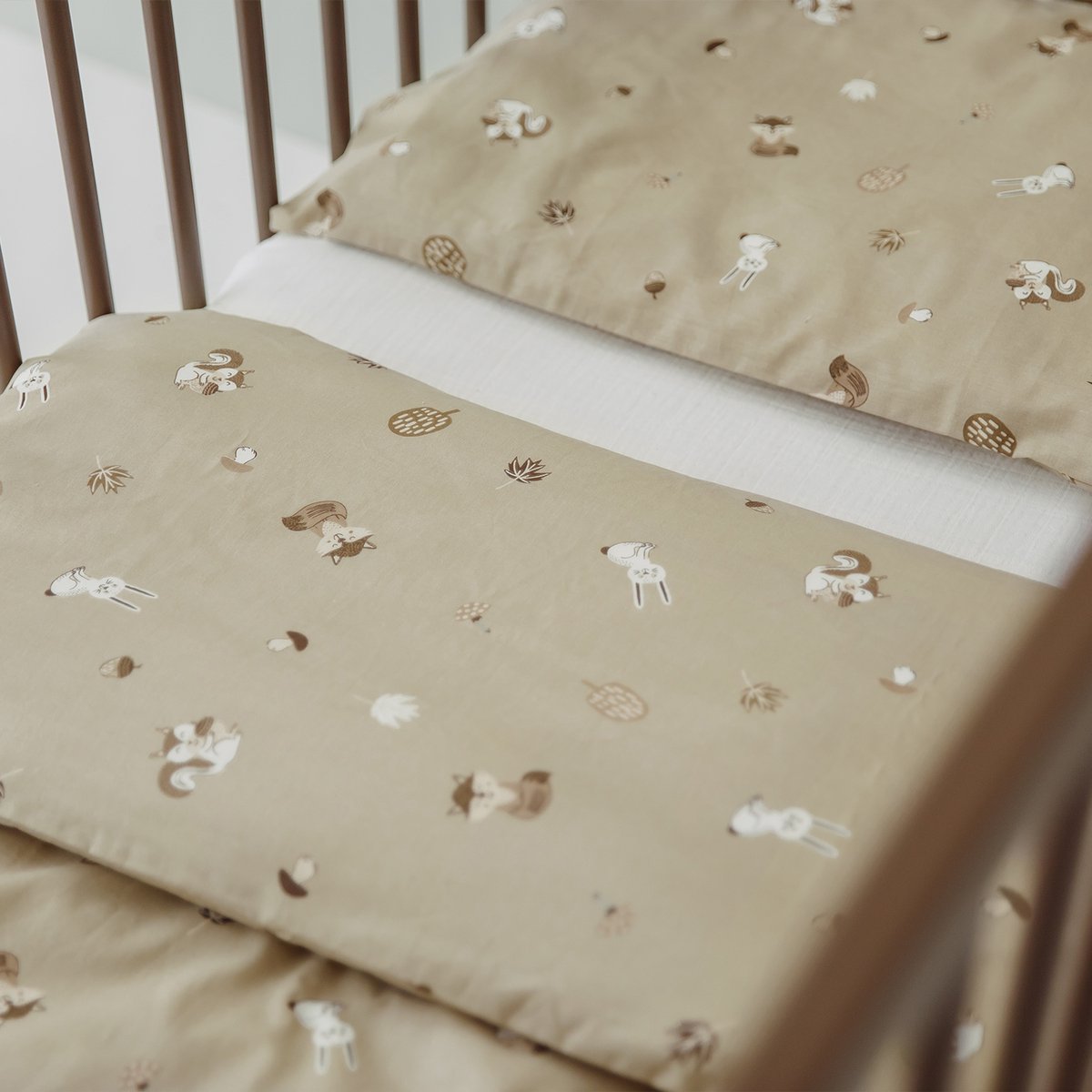 A bed with beige sheets and pillowcases featuring a pattern of unicorns, pineapples, acorns, and maple leaves.