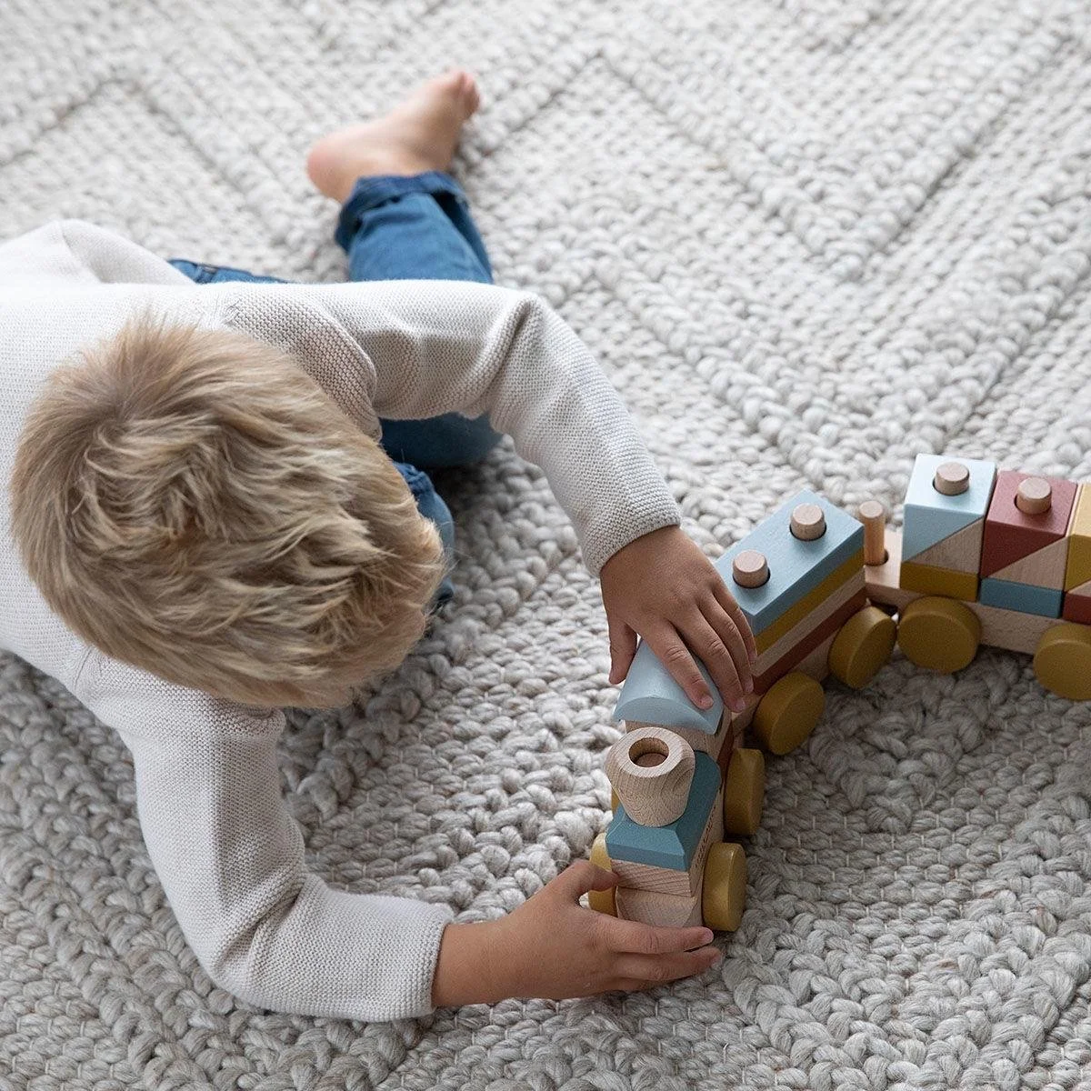Child playing with colorful wooden toy train on a textured beige carpet.