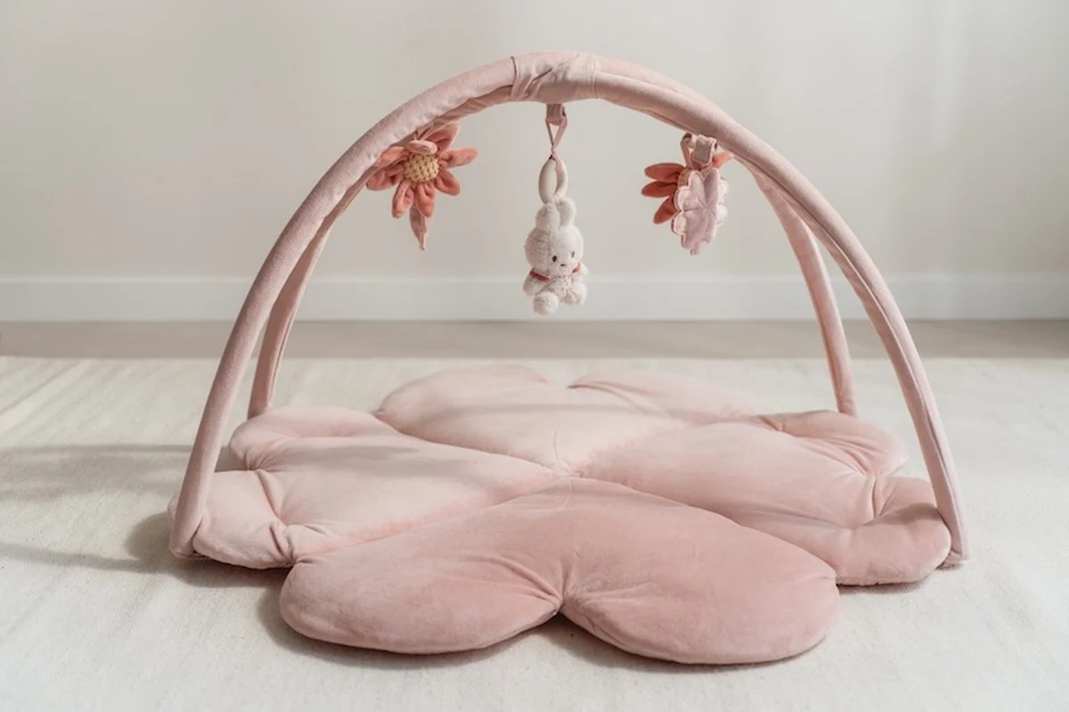 Soft pink baby play mat with cushioned flower-shaped pieces and a tiny hanging plush bunny toy underneath a pink arch