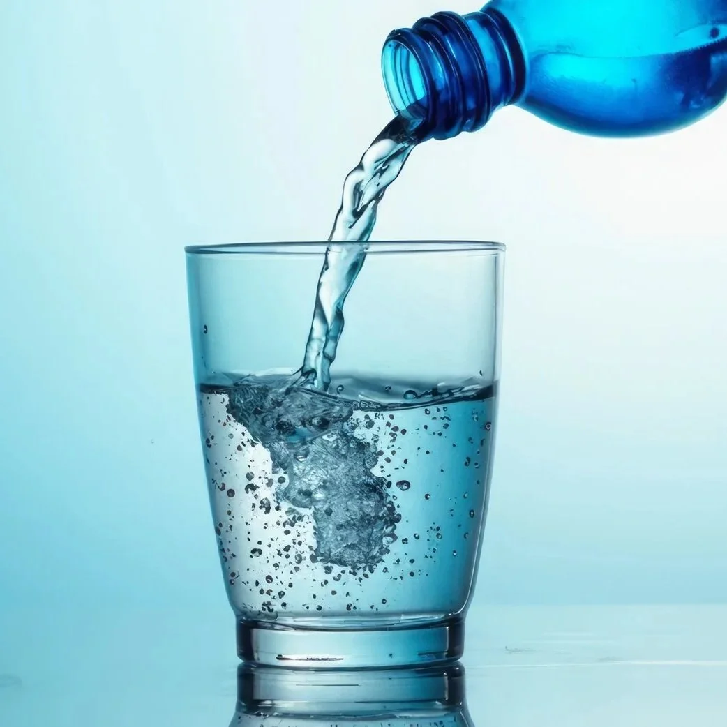 A close-up photo of water being poured from a blue plastic bottle into a clear glass, creating bubbles and waves.
