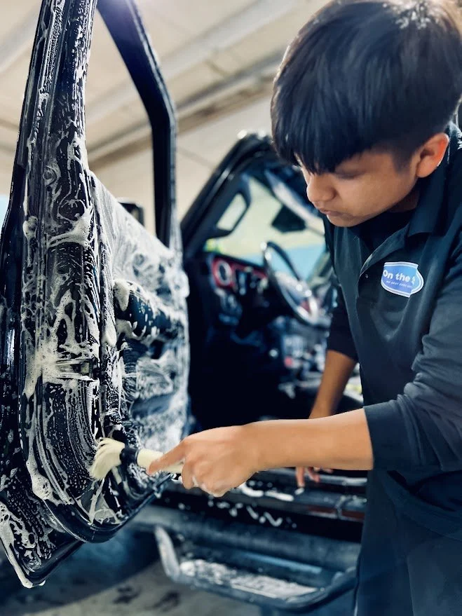 A person washing a car door with soap foam at a car wash station.