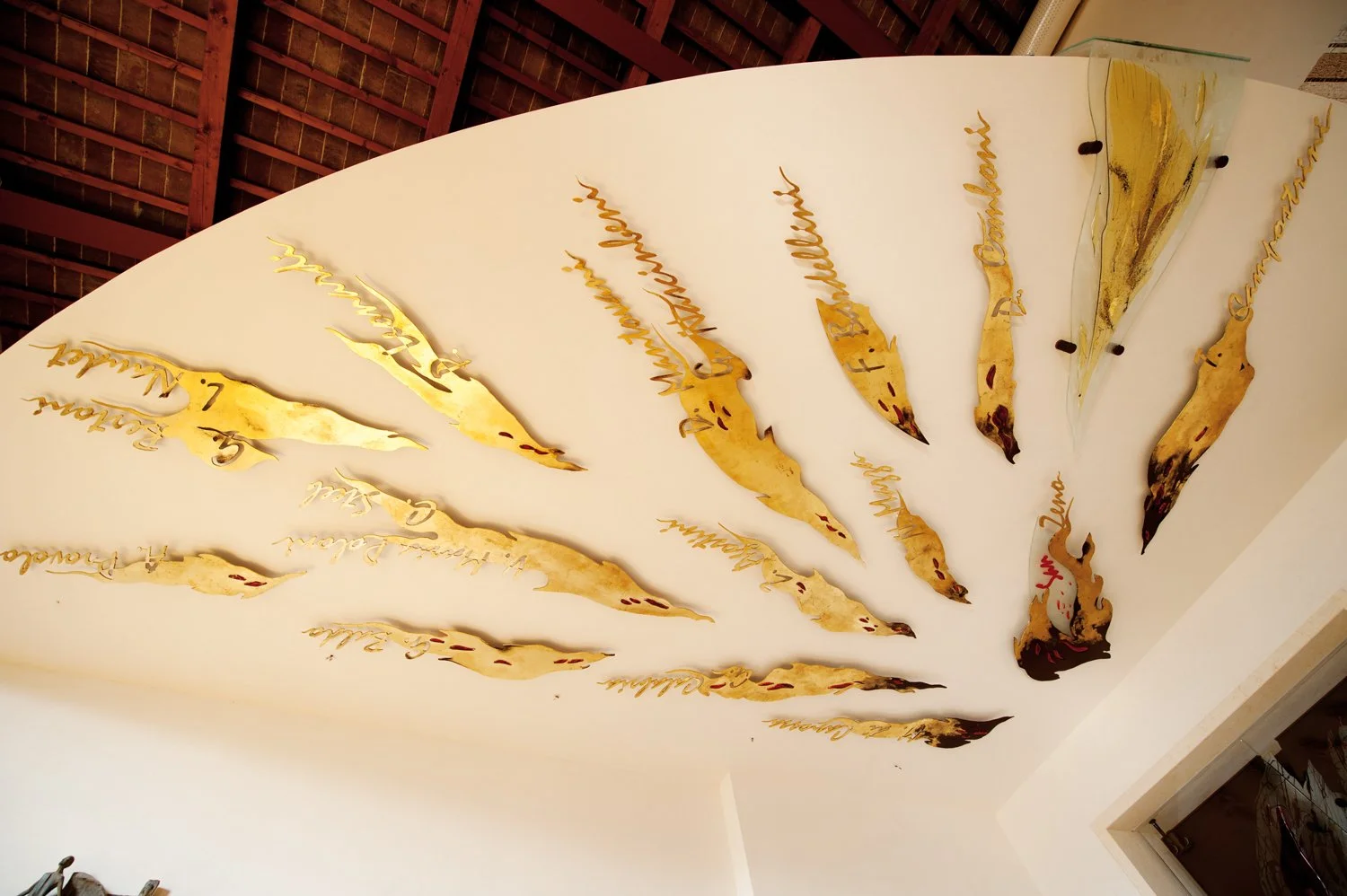 Decorative wall art featuring gold-colored, flame-shaped metallic cutouts with cursive handwriting, mounted on a white wall.