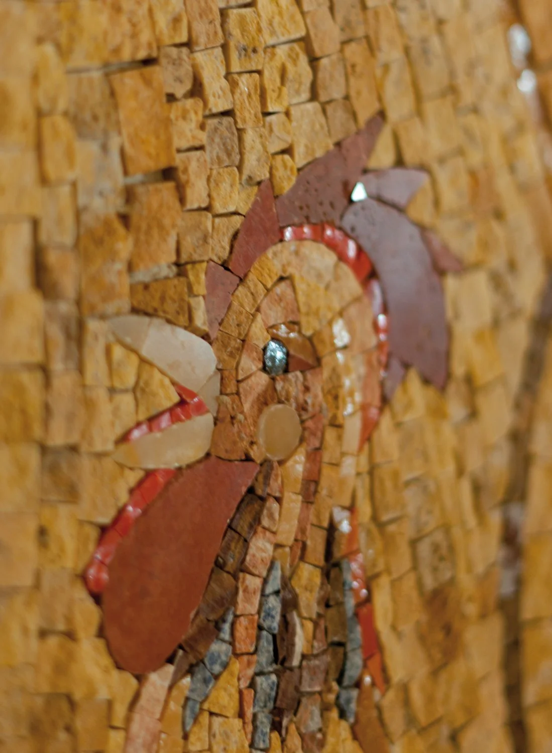 Close-up of a colorful mosaic artwork, featuring small, irregularly shaped tiles in warm earth tones, arranged in an abstract pattern.