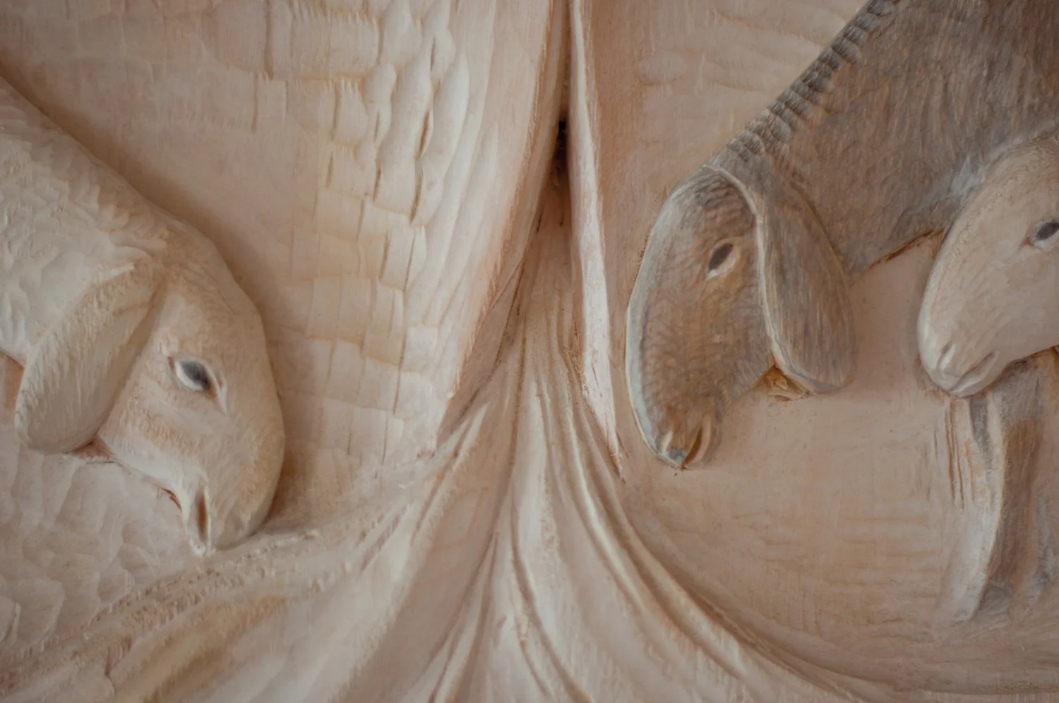 Close-up view of a detailed wooden carving featuring two faces, including eyes, noses, and mouths, with intricate wood grain textures.