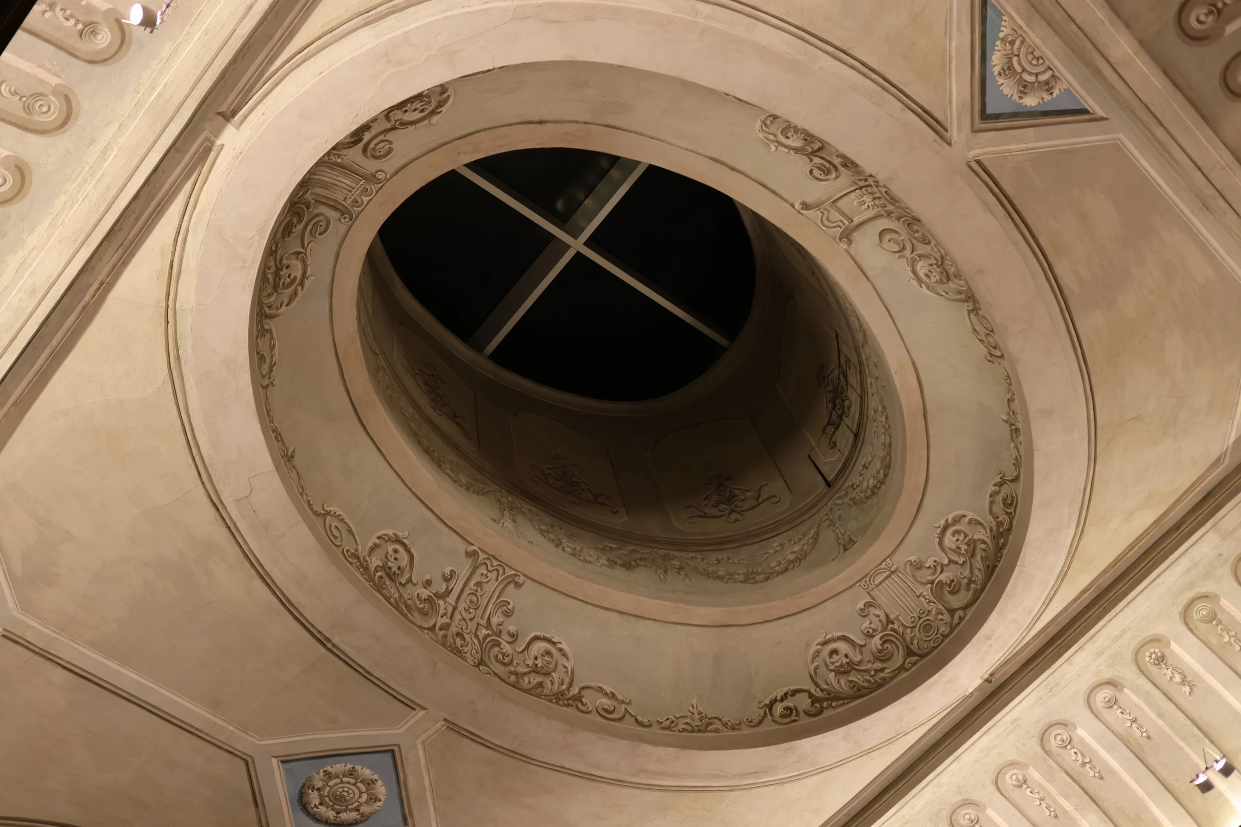 Interior view of a spiral staircase with ornate decorative moldings and paintings on the ceiling.