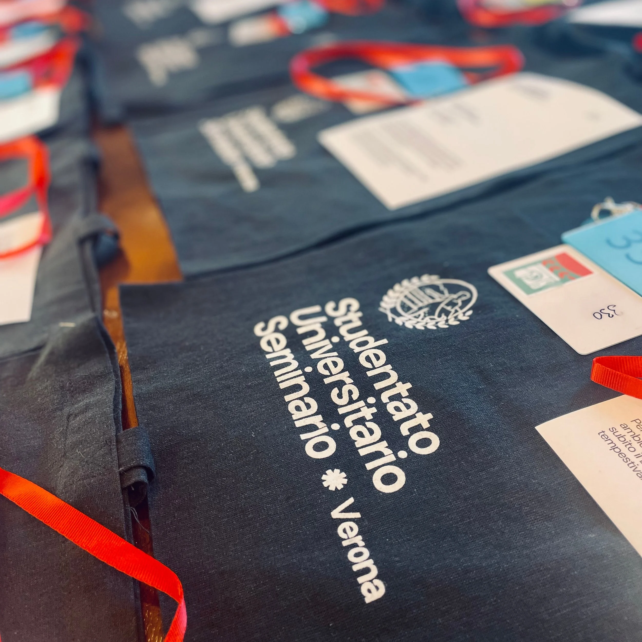 Close-up of a dark fabric bag with white text and logos, orange ribbon, and a blue card with text.