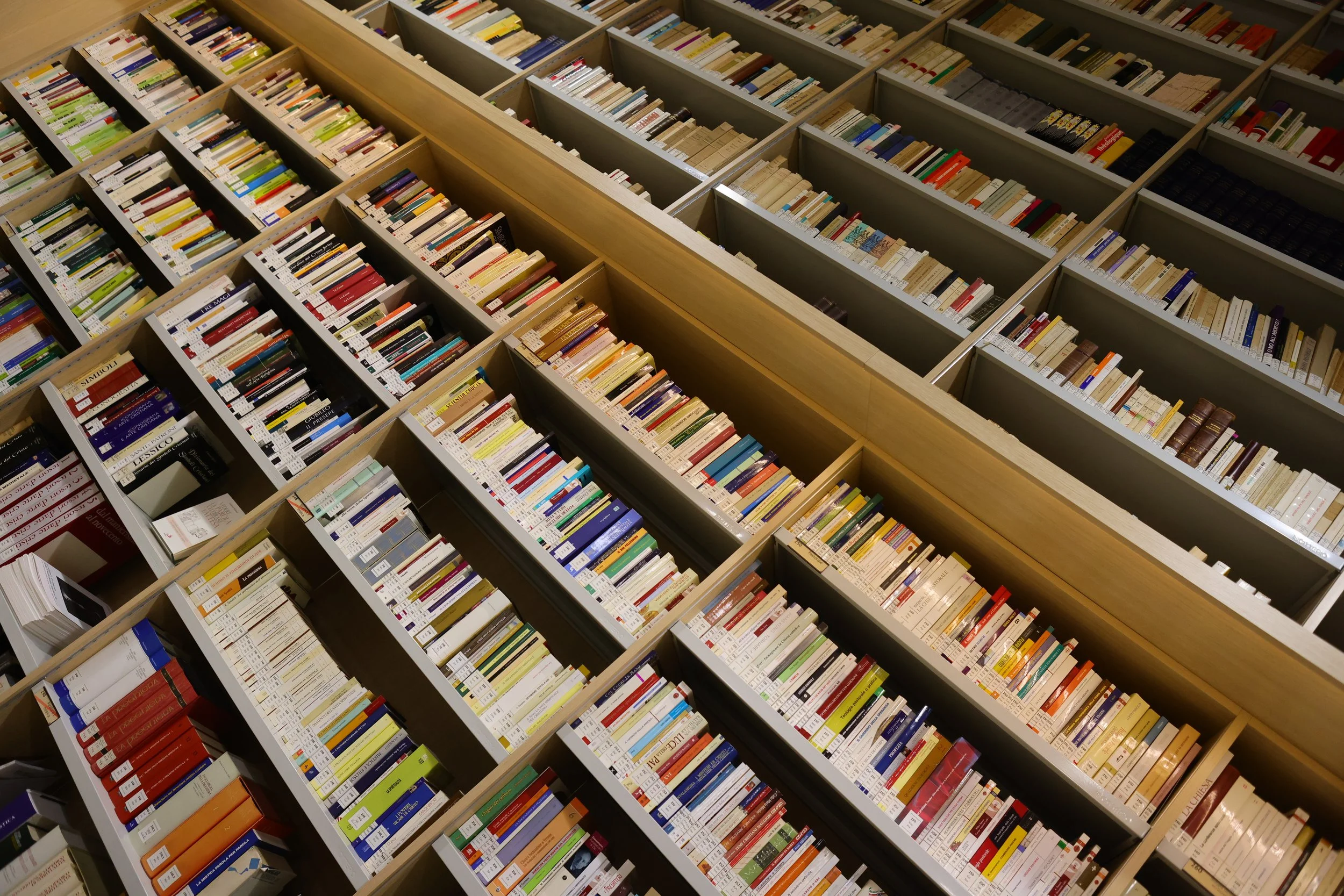 Multiple bookshelves filled with books at a bookstore or library, including a variety of colorful titles and labels.
