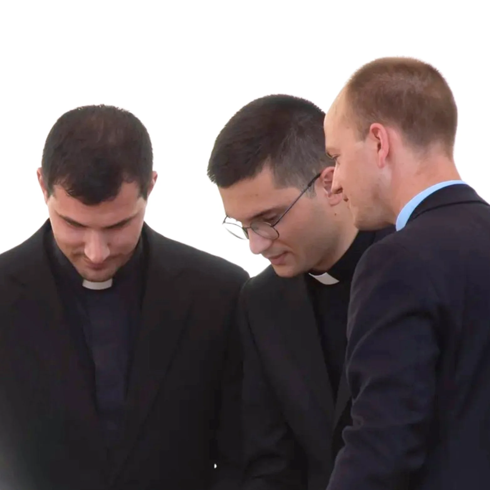 Three priests in clerical collars, one with glasses, gathered together looking down, against a plain white background.