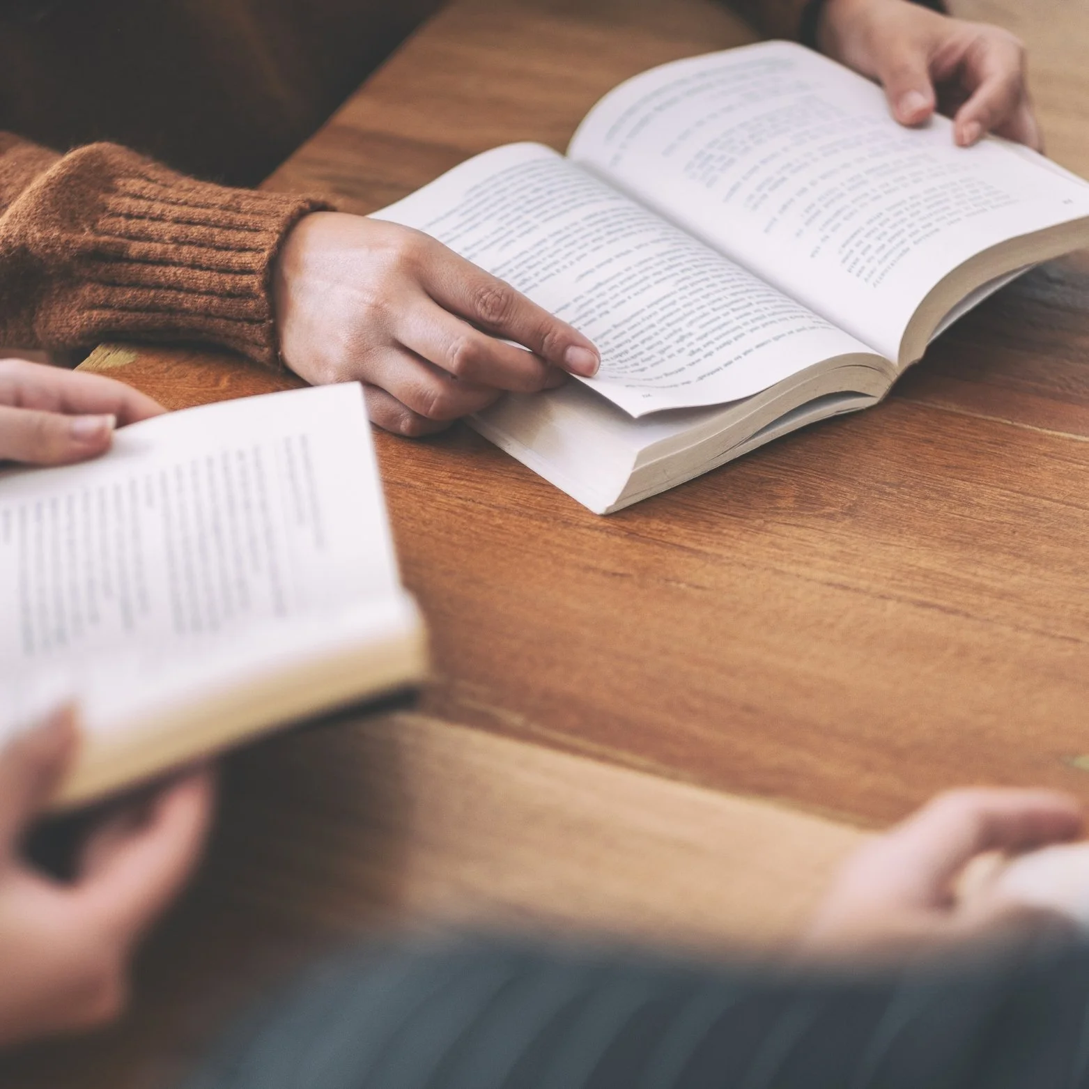 People sitting at a wooden table looking at open books.